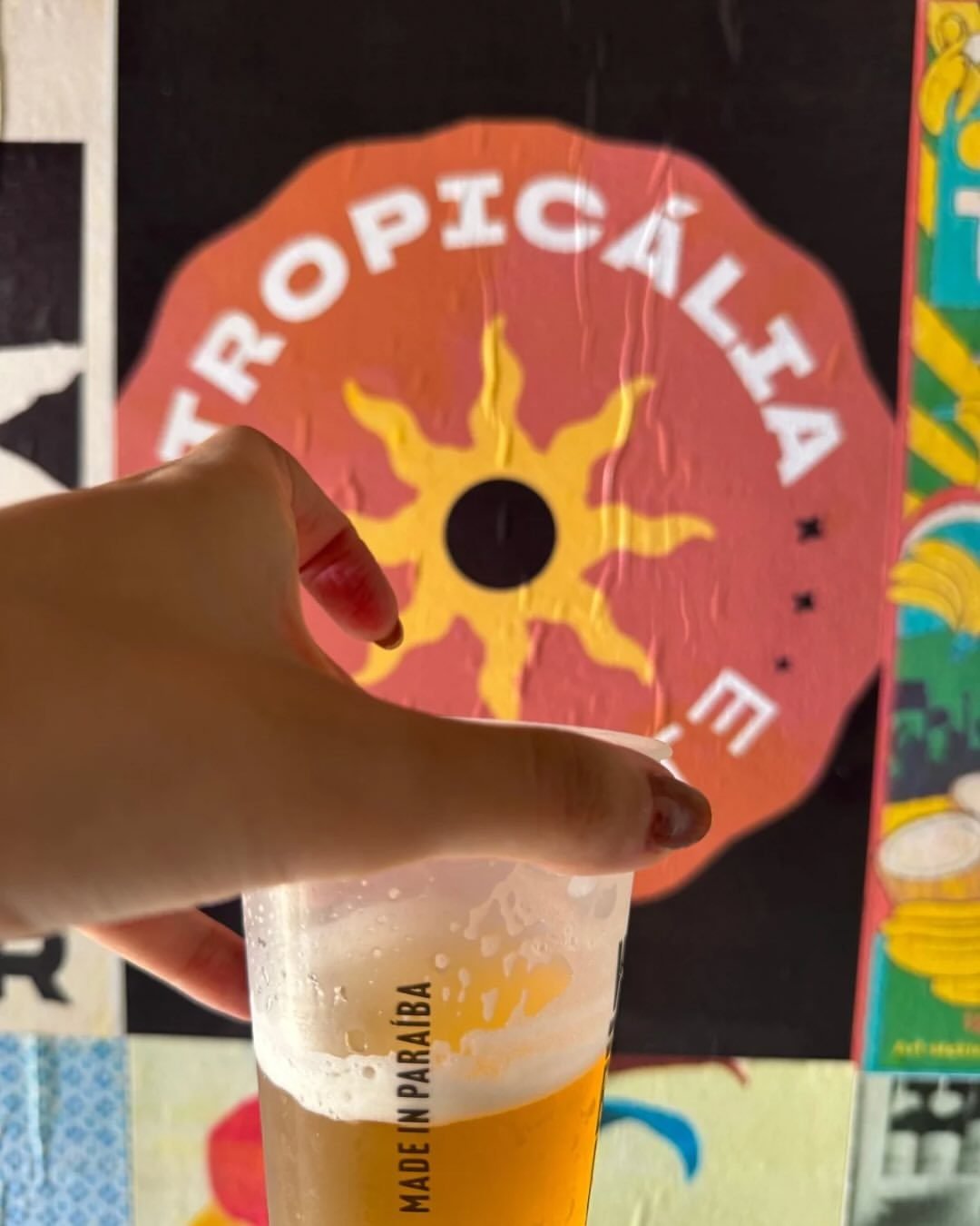 Copo de chopp em frente ao lambe-lambe com o sol do Tropicália Mutante